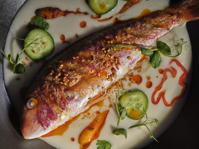 Vista superior de pescado frito en sartén con salsa con pepino y hierbas y especias - foto de stock