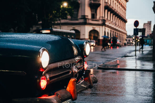 Hood of blue vintage car with lights on and red old car in motion on background on rainy weather in Cuba — Stock Photo