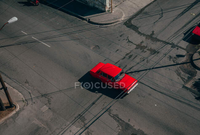 З верху асфальтової дороги перетинається з червоним вінтажним автомобілем серед сучасних транспортних засобів посередині Куби. — стокове фото