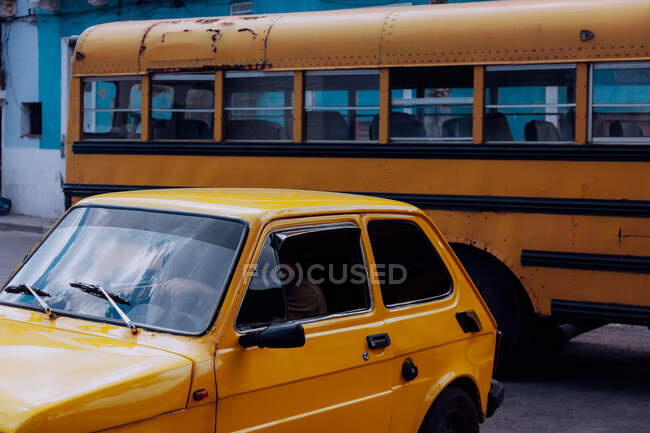 Coche vintage amarillo retro y autobús escolar amarillo en la calle de la ciudad con edificios antiguos - foto de stock