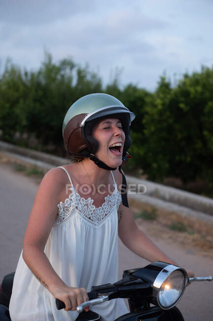 Allegro donna in vacanza in abiti leggeri sorridente con gli occhi chiusi sulla moto in movimento sulla strada — Foto stock