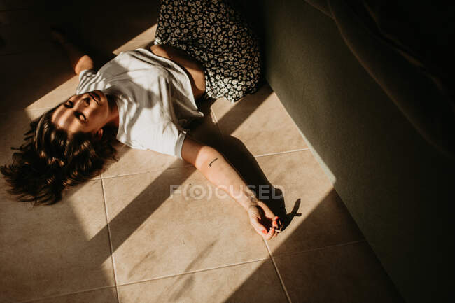 From above of tranquil woman lying on floor with spreader hands closed eyes and cigarette under rays of sun falling through window at home — Stock Photo