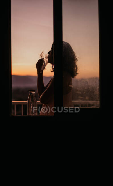 Vista lateral da silhueta jovem mulher sem rosto acendendo cigarro com magnífico pôr do sol no fundo borrado — Fotografia de Stock