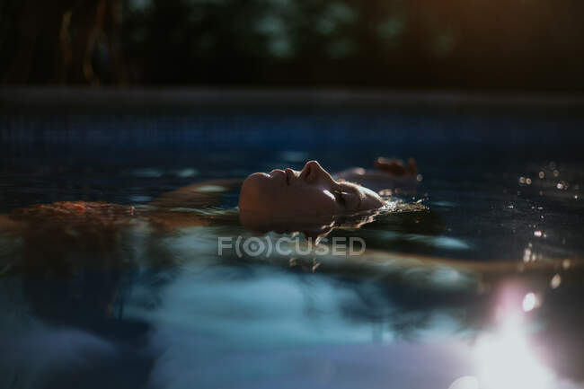 Side view of face above water surface of resting tranquil woman with closed eyes in swimming pool on sunny summer day — Stock Photo