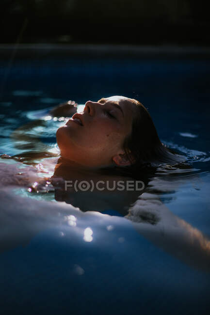 Side view of face above water surface of resting tranquil woman with closed eyes in swimming pool on sunny summer day — Stock Photo
