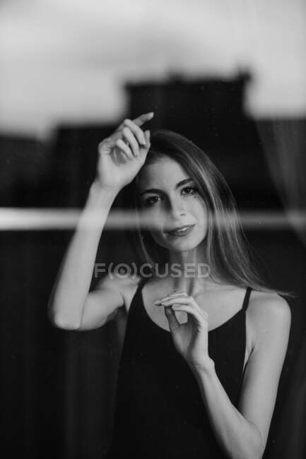 Charming elegant woman gracefully raising hands and looking at camera reflecting in city glass — Stock Photo