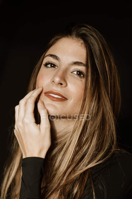 Sensual gorgeous woman in dark dress touching face and looking at camera — Stock Photo