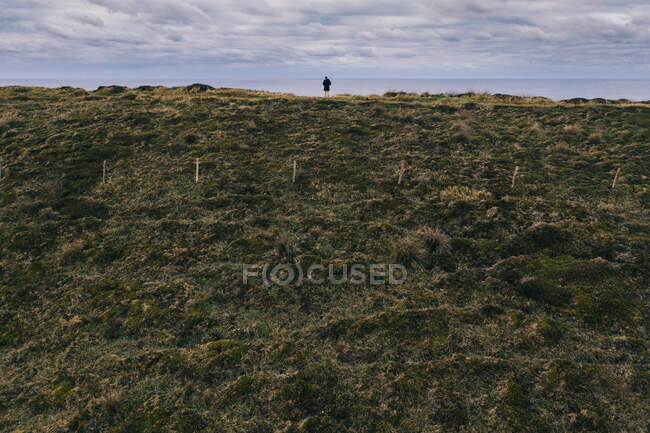 Vista posterior de la persona disfrutando del horizonte y el cielo nublado de pie al borde de en Pielagos, Cantabria, Santander, España - foto de stock