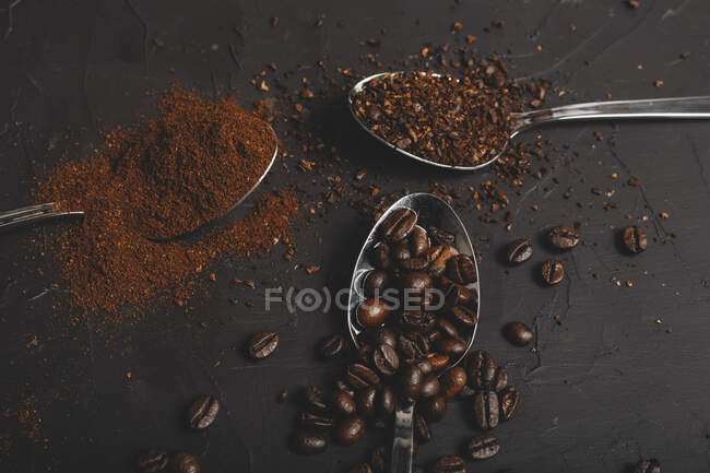 Tipos de café molido instantáneo y en polvo y granos de café en cucharas sobre mesa negra - foto de stock