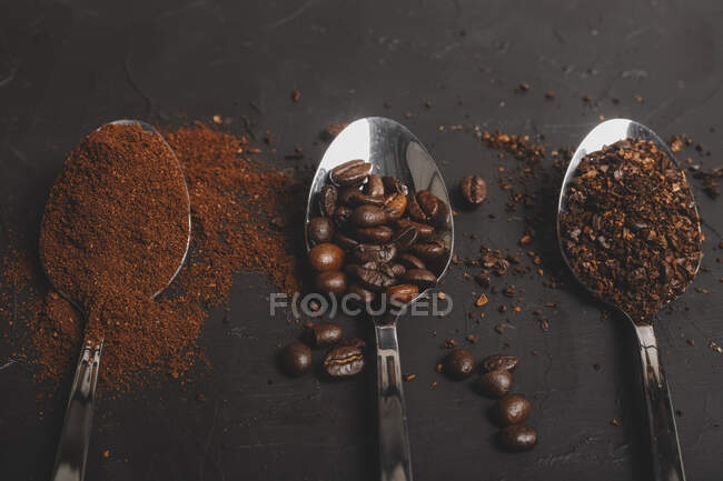 Tipos de grãos de café instantâneo e pó e café em colheres na mesa preta — Fotografia de Stock