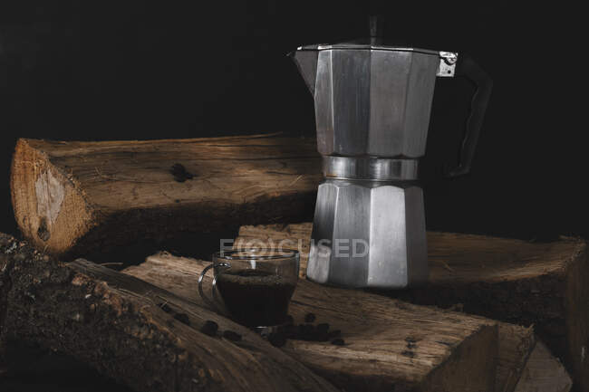 Tasse à café avec bouilloire et grains de café sur bois de chauffage isolé sur fond noir — Photo de stock