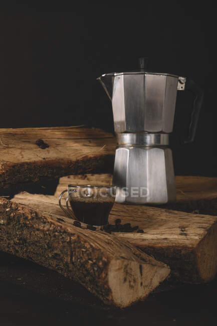 Mug of coffee drink with kettle and coffee beans on firewood isolated on black background — Stock Photo