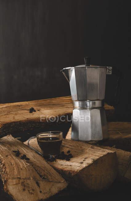 Mug of coffee drink with kettle and coffee beans on firewood isolated on black background — Stock Photo