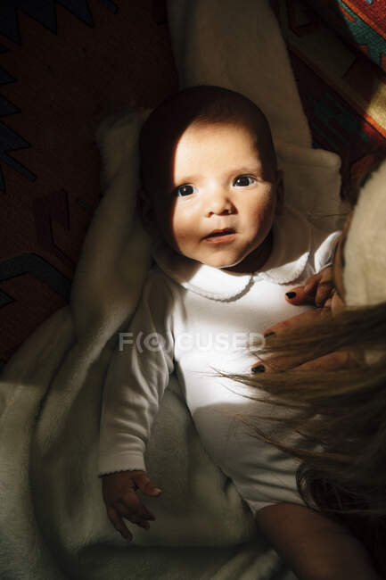 Von oben ein ruhiges Baby mit offenem Mund im Pyjama auf dem Bett liegend Mutter streichelt entzückenden Säugling und schaut in die Kamera — Stockfoto