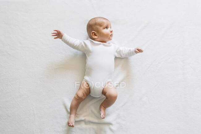 Vista dall'alto del bel bambino in pigiama bianco con bocca aperta sdraiato sul letto muovendo braccia e gambe guardando in alto — Foto stock