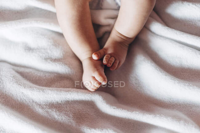 Zugeschnittene unkenntlich neugeborene Babyfuß liegt auf weißem Bett bewegt Beine zu Hause — Stockfoto