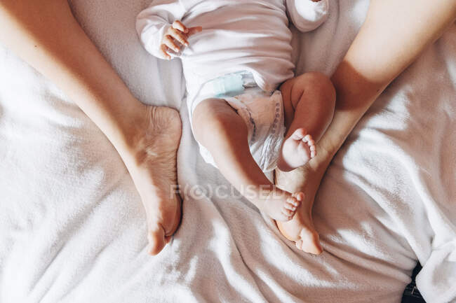 Вид сверху новорожденного ребенка в пеленке, лежащего на кровати с матерью в доме — стоковое фото