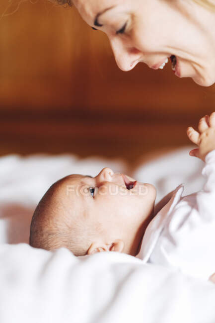 Gros plan de maman heureuse touchant nez par nez de bébé jouant avec le nouveau-né avec la bouche ouverte s'amusant couché sur le lit à la maison — Photo de stock