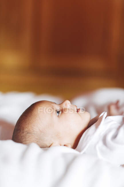 Calm adorable newborn infant in pajama lying on bed at home looking up — Stock Photo