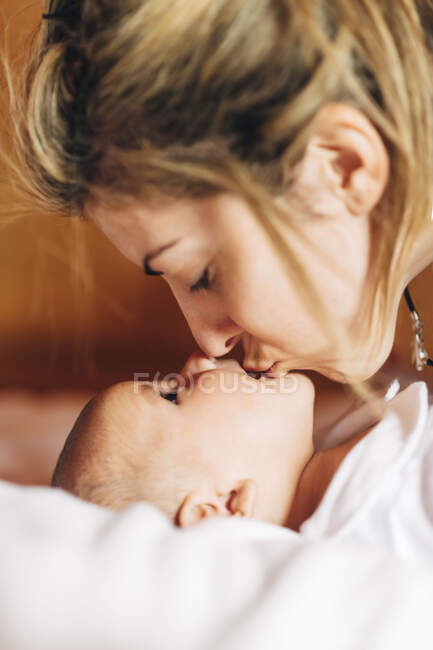 Close-up de mãe feliz tocando nariz por nariz do bebê brincando com o recém-nascido com a boca aberta se divertindo deitado na cama em casa — Fotografia de Stock