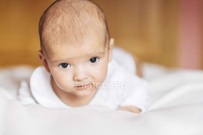 Calm adorable newborn infant in pajama lying on bed at home looking at camera — Stock Photo