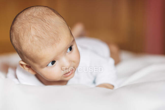 Ruhiges liebenswertes Neugeborenes im Pyjama zu Hause auf dem Bett liegend und wegschauend — Stockfoto