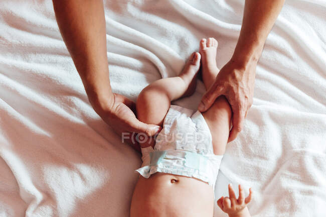 Top view of dad touching legs of newborn infant in diaper lying on bed in house — Stock Photo