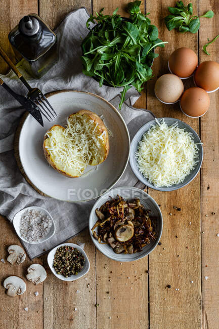 Vista superior de papas rellenas sobre mesa de madera con champiñones fritos queso rallado y hierbas - foto de stock