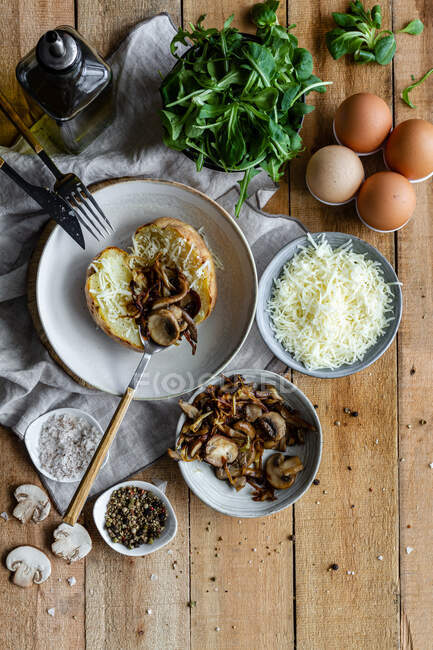 Draufsicht auf gefüllte Kartoffeln auf Holztisch mit gebratenen Champignons geriebenem Käse und Kräutern — Stockfoto