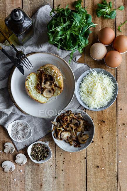 Top view of stuffed potato on wooden table with fried mushrooms grated cheese and herbs — Stock Photo