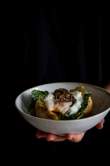 De arriba del cuenco blanco cerámico con las setas sabrosas fritas de huevo las hierbas en la patata por la mano de cultivo - foto de stock