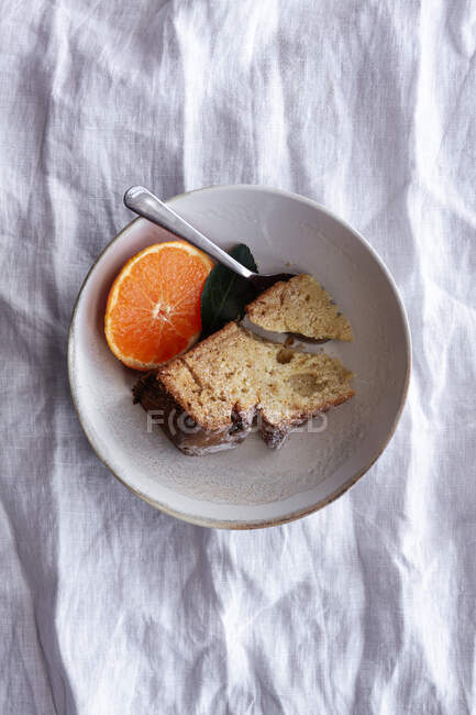 De arriba apetitoso pastel dulce y mandarina naranja madura cortada y servida en plato blanco en la mesa - foto de stock