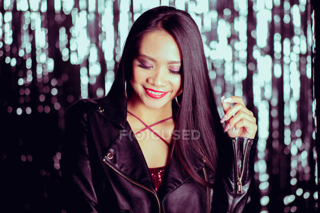 Glamorous long haired asian woman looking down with smile on background of sparkling wall — Stock Photo