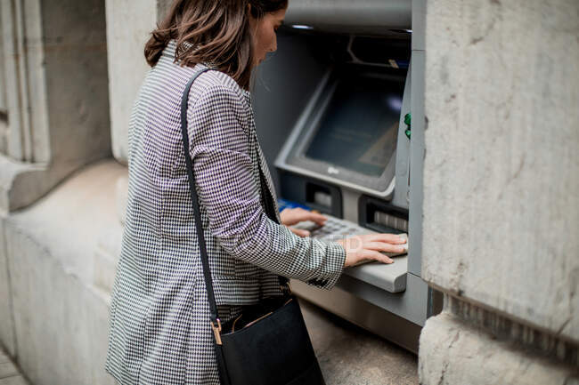 Vista lateral da senhora de cabelos pretos bem vestida inserindo cartão de crédito para ATM — Fotografia de Stock