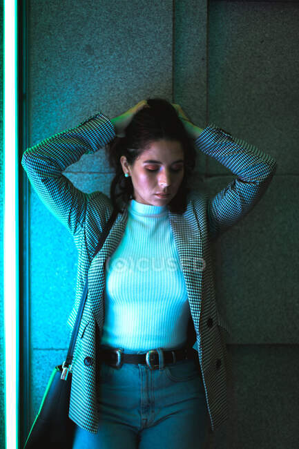Female teenager in casual jeans and grey jacket standing and shaking head with waving black hair in neon light — Stock Photo
