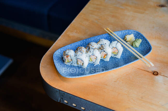 Desde arriba de rollos asiáticos con arroz verduras salsa verde wasabi jengibre y palillos de madera en elegante plato azul - foto de stock