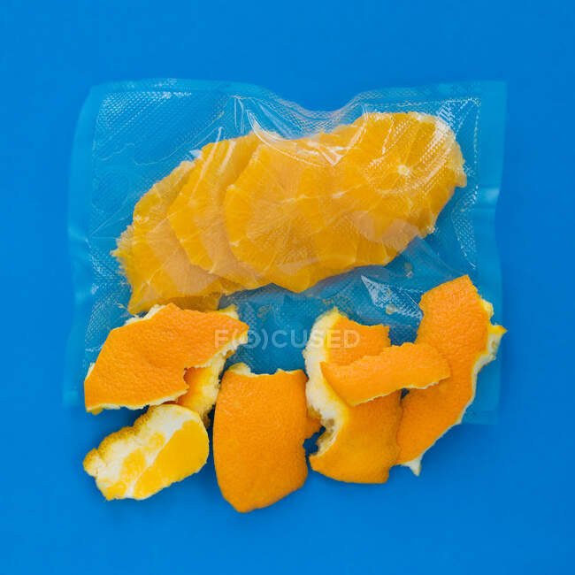 Top view of ripe peeled orange in vacuum plastic bag and orange peel on blue background — Stock Photo