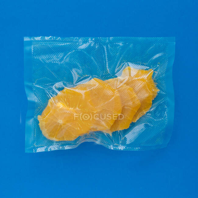 Draufsicht auf reife geschälte Orange in Vakuum-Plastiktüte auf blauem Hintergrund — Stockfoto