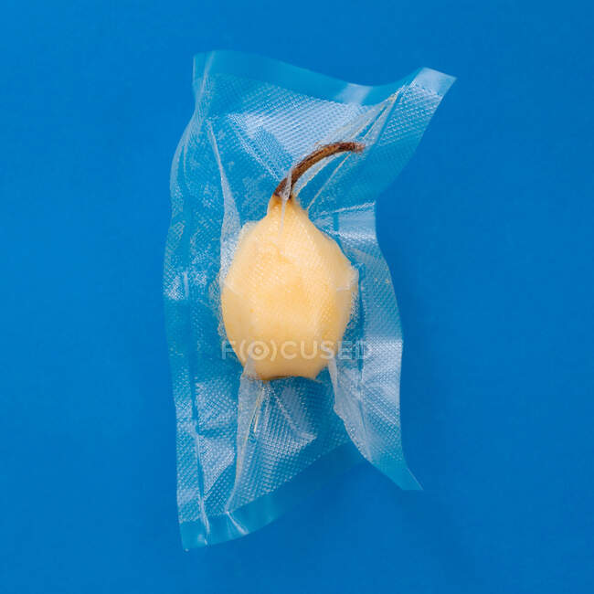 Top view of ripe yellow peeled pear in vacuum plastic bag on blue background — Stock Photo