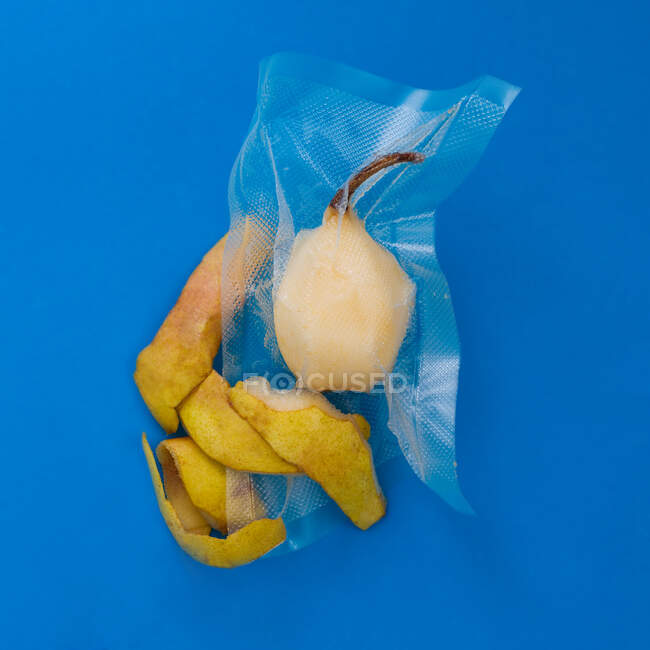 Top view of ripe yellow peeled pear in vacuum plastic bag and pear peel on blue background — Stock Photo