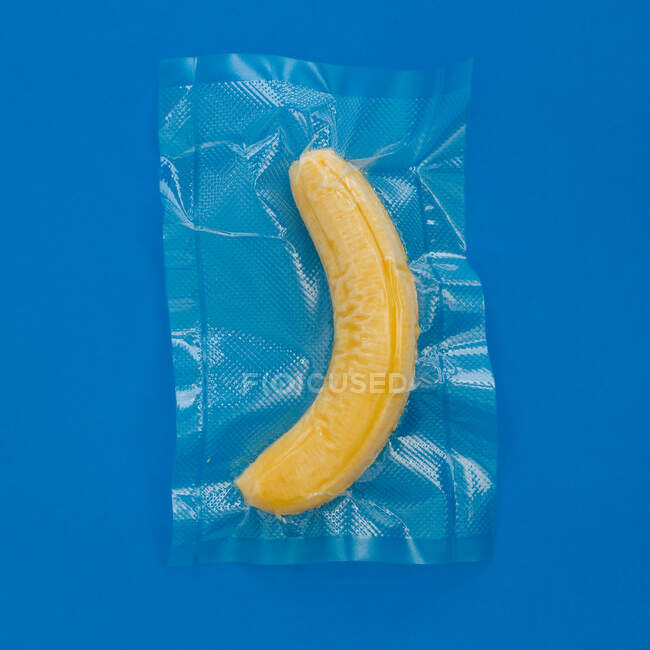Top view of ripe yellow peeled banana in vacuum plastic bag on blue background — Stock Photo