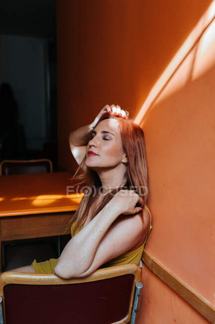 Зверху червоноголові жінка сміється з закритими очима, відпочиваючи на стільці на сучасній кухні. — стокове фото