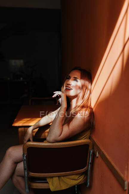 Side view of thoughtful model in stylish yellow dress with makeup sitting on chair and looking away — Stock Photo