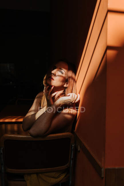 Вид сбоку на прекрасную модель в стильном желтом платье с макияжем, сидящую на стуле и отводящую взгляд — стоковое фото