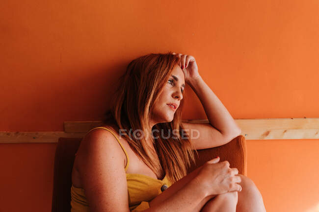 Side view of thoughtful redhead woman looking away while resting on chair at home — Stock Photo