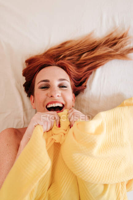 Vue du dessus de surprise rousse drôle de femme souriante tout en regardant sous la couverture jaune à la maison — Photo de stock