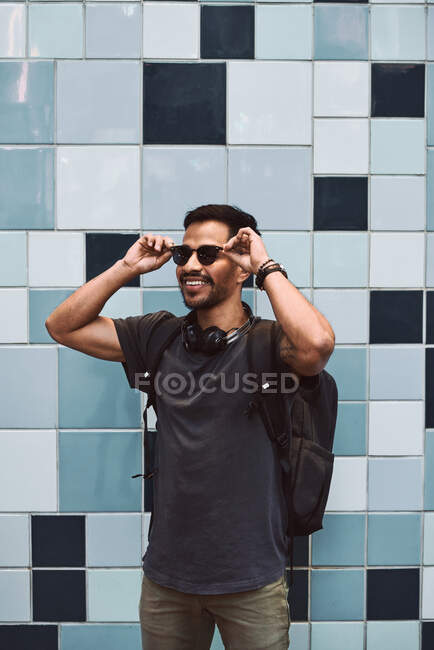 Homem hispânico feliz em roupas casuais e mochila com fones de ouvido em pé ouvindo música na rua da cidade — Fotografia de Stock