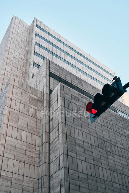 Desde abajo de semáforo negro con color rojo y edificio moderno con arquitectura creativa bajo el cielo azul en el fondo - foto de stock