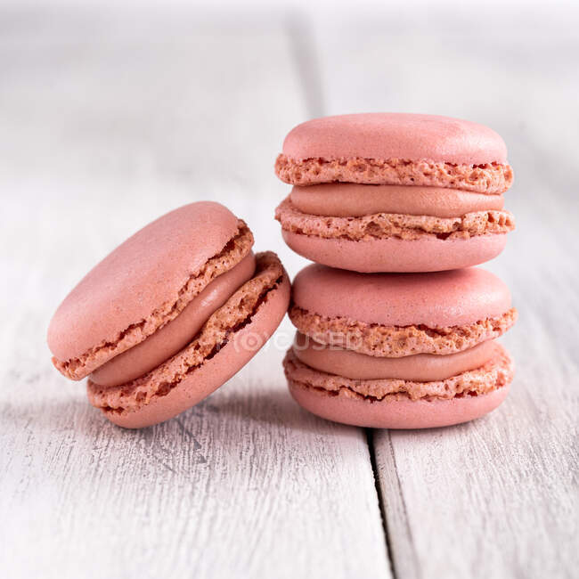 Pink tasty macaroons stacked in pile against wooden white surface — Stock Photo
