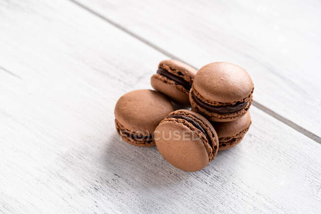 Brown tasty macaroons stacked in pile against wooden white surface — Stock Photo